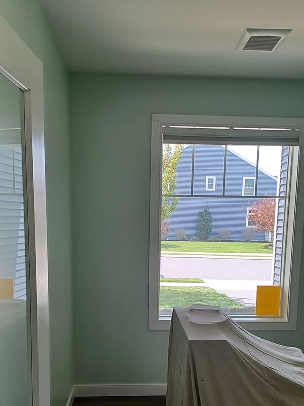 Freshly painted mint green room with framed window and covered furniture