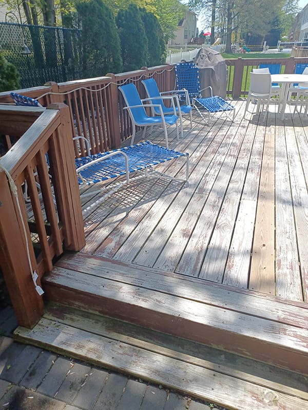 Faded wooden deck with railings and outdoor seating before staining