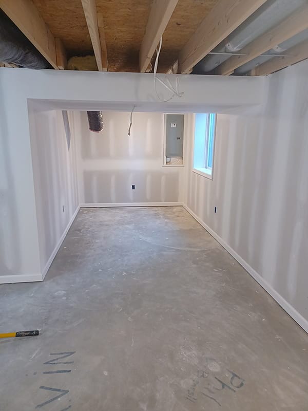 Unfinished basement room with taped drywall walls and concrete floor