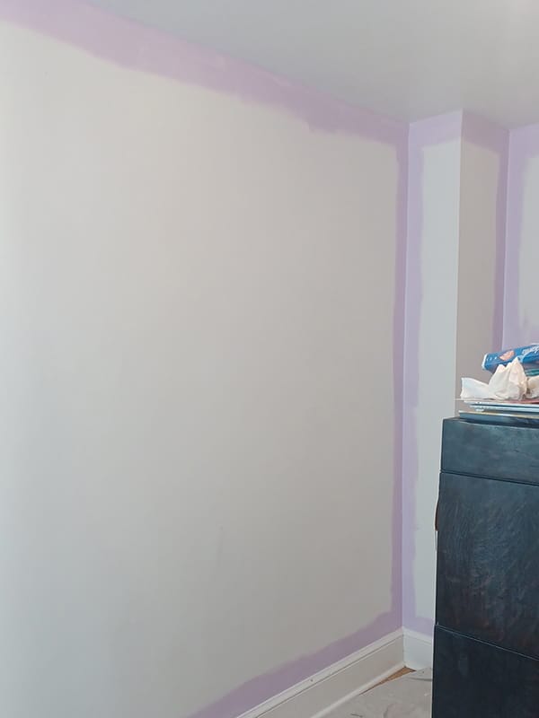 Bedroom wall being primed and cut-in with purple paint border